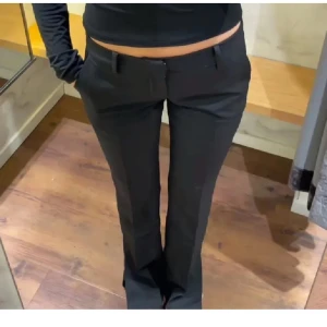 Svarta kostymbyxor - Snygga svarta kostymbyxor med låg midja och bootcut-stil. Perfekta för en stilren look. Byxorna har en klassisk design med knappar och dragkedja framtill.