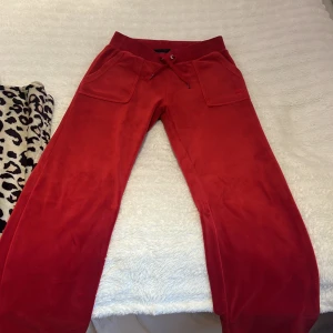 Röda mjukisbyxor från Juicy Couture - Snygga röda mjukisbyxor från Juicy Couture med snörning i midjan och praktiska fickor fram. Perfekta för en avslappnad stil. Byxorna har en mjuk och bekväm känsla och är i storlek XS, hela och fina!