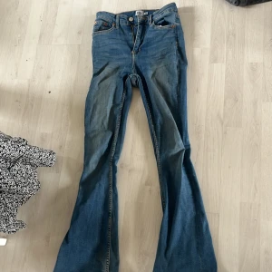 Blå bootcut jeans - Snygga blå bootcut jeans med klassisk femficksdesign och knappgylf. Perfekta för en avslappnad stil med en touch av retro. Passar bra till både sneakers och klackar.