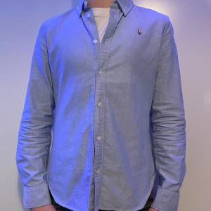 Ljusblå skjorta från Ralph Lauren - Nu säljer jag denna ljusblåa Ralph Laurent skjortan i storlek 16. Jag är 165 CM lång och den är för liten för mig. Jag rekommenderar att ha den om man är runt 158 CM lång. Den passar perfekt till sommaren och våren och den har inga hål eller fläckar på sig. Skick är 8/10 och jag har änvänt den några få gånger. Nypris är cirka 1500kr och mitt pris 380kr. Den är såklart riktig.  Hör av dig om du vill ha fler bilder eller något annat viktigt.