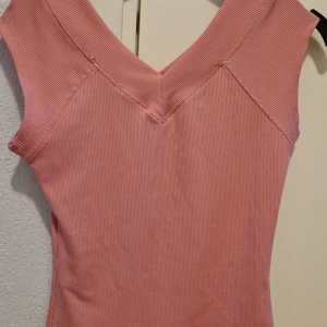 Rosa ribbad topp från Shein - Säljer en söt rosa ribbad topp från Shein. Toppen är ärmlös med en v-ringad design som ger en stilren look. Perfekt för varma dagar eller som ett lager under en jacka.