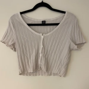 Vit ribbad kortärmad topp - Säljer en söt vit ribbad topp. Den har korta ärmar och knappar framtill. 