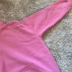 Rosa hoodie - Säljer en snygg rosa hoodie med känguruficka och justerbar huva. Perfekt för en avslappnad stil. Passar bra till jeans eller leggings. Hör av dig vid intresse! 💖(finns ett litet hål, se bilder)