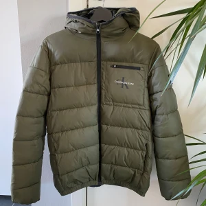 Olivgrön pufferjacka från Calvin Klein - Säljer en olivgrön vinterjacka ifrån Calvin klein eftersom den blivit för liten..jackan är använd men finns inga märken eller liknande utan är som ny!är storlek 170 o passar personer runt 165-175..kan säljas billigare vid snabb o smidig affär!
