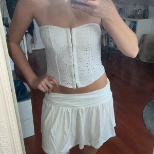 Vit korsett med spetsdetaljer - Säljer en stilren vit korsett med vackra spetsdetaljer och knäppning fram. Perfekt för att ge en elegant touch till din outfit. Passar bra till både kjol och byxor. Off shoulder, snygg till sommaren