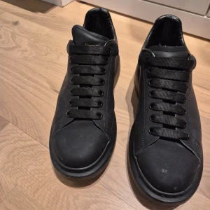 Svarta sneakers från Alexander McQueen - Snygga svarta sneakers från Alexander McQueen med klassisk design och snörning. Skorna har en rund tå och är tillverkade i skinn med subtila detaljer i guld på hälen.