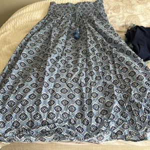 Blå mönstrad klänning från Gina Tricot - Säljer en blå klänning från Gina Tricot med ett snyggt mönster i vitt och mörkblått. Klänningen har en smockad överdel och dekorativa tofsar framtill. Perfekt för en somrig look! 🌸