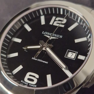 Longines Conquest klocka - Säljer en stilren Longines Conquest klocka med svart urtavla och datumvisning. Klockan har en silverfärgad boett och armband i rostfritt stål. Vattentät upp till 300 meter och kommer med originalförpackning och manual.
