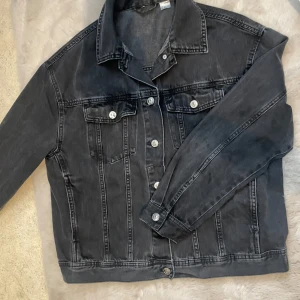 Svart jeansjacka - Säljer en stilren svart jeansjacka från Zara. Jackan har en klassisk design med knappar framtill och två bröstfickor med lock. Perfekt för en avslappnad look.