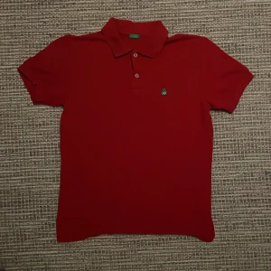 Röd pikétröja med broderad logga - Säljer en snygg röd pikétröja med en grön broderad logga på bröstet. Tröjan har korta ärmar och en klassisk krage med knappar. Perfekt för en stilren och avslappnad look.                                                       Original priset är 549