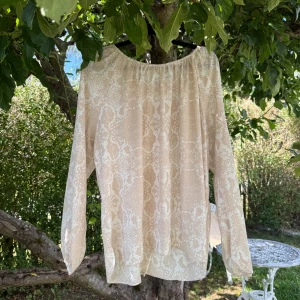 Beige blus med ormmönster från Cream - Säljer en luftig och snygg beige blus från Cream i storlek 44. Blusen har ett diskret ormmönster i vitt och beige, rundad hals och långa ärmar med lätt puff. Blusen har också en halvt öppen rygg. Materialet känns mjukt och faller fint, perfekt för dig som gillar chill och stilren vibe. Mycket fint skick, jag hittar inga synliga anmärkningar eller defekter.