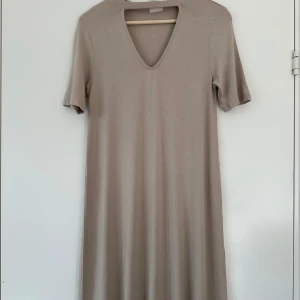 Beige klänning M/L - Superskön beige knälång klänning med kort ärm och en V-formad halsringning med cutout. Mjukt och härligt viskosmaterial som andas, så perfekt även riktigt varma dagar. Storlek M/L.   Legat i garderoben ett år, så nästan nyskick.   Hämtas i Stockholm eller skickas mot porto. 