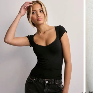 Svart slim topp med v-ringning - Snygg svart topp med v-ringad hals och korta ärmar. Slimmad passform som framhäver figuren och har en diskret spetskant vid halsen. Perfekt att matcha med jeans eller kjol för en cool och enkel look.