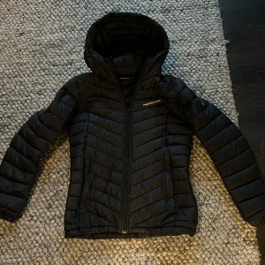 Svart dunjacka Peak Performance S - Svart dunjacka från Peak Performance med huva och dragkedja som är en perfekt höst och vinter jacka i storlek S