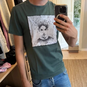 Grön Limitato t-shirt med tryck - Snygg grön t-shirt från Limitato med ett stort vitt tryck på bröstet som har ett konstnärligt motiv i svart. T-shirten har rund hals och korta ärmar, tillverkad i mjuk bomull. Perfekt för dig som gillar unika prints och stilren design. Priset är inte hugget i sten!