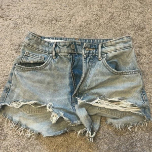 Blå jeansshorts med fransar från Zara - Snygga blå jeansshorts från Zara i storlek 34. slitna detaljer och fransig kant nedtill. Perfekta för varma dagar. Dragkedja och knapp framtill. Inte andvända mycket eftersom att jag köpte de för små och knappt kunde andvända