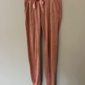 Rosa mjukisbyxor med band - Supermysiga rosa mjukisbyxor i sammetsliknande material med bred resår i midjan och knytband. Byxorna har fickor på sidorna och smala ben med muddar nertill. Perfekta för chill eller hemmakvällar.