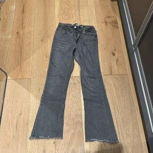 Grå bootcut jeans från ONLY - Snygga grå jeans från ONLY i bootcut-modell med råa, fransiga benslut. Klassisk femficksdesign och knappstängning framtill. Jeansen har en mörkgrå ton och är tillverkade i mjukt jeansmaterial som sitter skönt. *Sytt in resår gummiband innanför ryggen så att byxorna sitter bättre. 