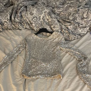 Silver paljettopp med öppen rygg Amisu - Säljer en glittrig silverfärgad paljettopp från Amisu i storlek XS. Toppen har lång ärm, croppad passform och en snygg öppen rygg. Perfekt för dig som vill sticka ut med extra bling! Materialet är polyester med paljetter över hela ytan,perfekt att ha på nyår eller när det sker festande.