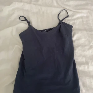 Mörkblå linnetopp med smala axelband - En stilren mörkblå linnetopp med smala justerbara axelband och mjuk V-ringning. Toppen är ärmlös och har en enkel, clean design som passar perfekt till jeans eller kjol. Materialet känns lätt och bekvämt mot huden.