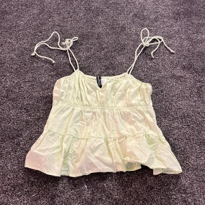 Ljusgrön linnetopp från H&M Divided - Supersöt ljusgrön linnetopp från H&M Divided med tunna axelband som knyts och volangdetaljer nedtill. Toppen har en luftig och flowy passform, perfekt för varma dagar. Materialet är mjukt och har en lätt glansig finish som ger en fräsch vibe. Aldrig använt!❤️