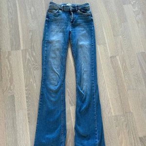 Blå bootcut jeans från ONLY - Snygga blå jeans från ONLY med bootcut-modell och klassisk femficksdesign. Jeansen har en lätt tvättad look och normal passform. Tillverkade i mjukt denimtyg med sköna stretchiga detaljer. Perfekta för dig som gillar retrovibbar och stilren denim.