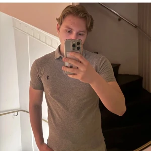 Grå piké från Polo Ralph Lauren - Slim fit grå pikétröja från Polo Ralph Lauren med klassisk krage och två knappar framtill. Diskret broderad logga i svart på bröstet. T-shirten är kortärmad och har en stilren look som funkar till jeans eller shorts. Passar även S