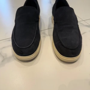 Mörkblå mockaloafers från Zara - Snygga loafers från Zara i mörkblå mocka med krämfärgad platt sula. Skorna har bara används en gång och har inga tecken på defekter Skorna har en stilren och enkel design med rund tå och slip-on modell, perfekt för dig som gillar en clean look. Passar dig som vill ha något bekvämt och samtidigt stilfullt.