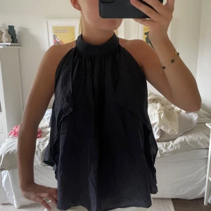 Mörkblå halterneck blus med hög krage - Säljer en mörkblå blus med halterneck och hög krage. Toppen har en luftig och flowy passform med snygga veck framtill. 