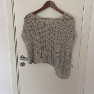 Beige stickad croppad topp - Säljer en beige stickad topp med grovt hålmönster och croppad passform. Toppen har en avslappnad, loose siluett och är perfekt för lager-på-lager. Den är ärmlös och har en snygg asymmetrisk nederkant.