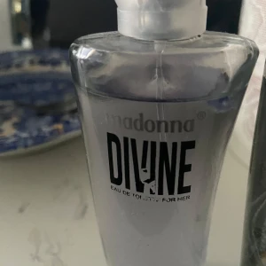 Madonna Divine Eau de Toilette - Fräsch och modern parfym från Madonna, Divine Eau de Toilette for Her. Flaskan är transparent med en silvrig ton och har en stilren, kantig form. Perfekt för dig som gillar en elegant och enkel design på din parfymhylla.