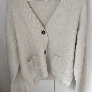 Beige kofta från Uniqlo med fickor - Säljer en beige kofta från Uniqlo i storlek M. Koftan har två framfickor, ribbade muddar och v-ringad hals med knappar framtill. Materialet är mjukt och stickat, perfekt för lager-på-lager. Enkel och clean design som funkar till allt.