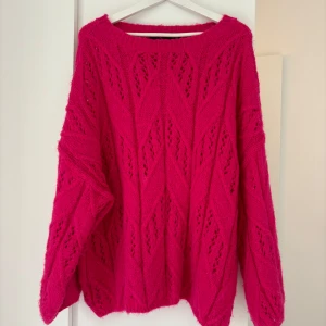 Rosa stickad tröja från Vero Moda - Säljer en oversized stickad tröja från Vero Moda i en stark rosa färg. Tröjan har ett snyggt hålmönster och bred halsringning. Den är långärmad och har en loose passform, perfekt för att mysa i under hösten och vintern.