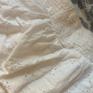 Vit kort klänning från Gina Tricot - Supersöt vit klänning från Gina Tricot i storlek 146/152. Klänningen har smock upptill och broderade blommor över hela tyget. Den är kort och har en luftig, volangig kjol som ger en chill och somrig vibe. Perfekt för dig som gillar romantiska detaljer och ljusa färger.