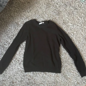 Svart stickad tröja från Gina Tricot - En enkel och stilren svart stickad tröja från Gina Tricot. Tröjan har rund hals, långa ärmar och ribbade muddar vid hals, ärmslut och nederkant. Perfekt att matcha med jeans eller kjol för en clean look.