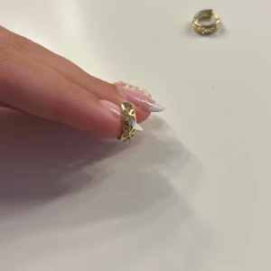 Guldiga örhängen med stenar - Säljer ett par små, runda örhängen i guldton med infällda glittrande stenar. De har en snygg, klassisk design som ger en lyxig vibe och passar perfekt om du vill addera lite bling till din look.