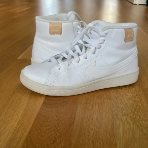 Vita Nike sneakers strl 37.5 - Säljer ett par fräscha vita Nike sneakers med högt skaft och klassisk snörning. Andvända runt en till två gånger 