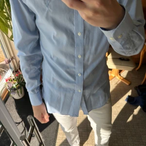 Ljusblå skjorta från Ralph Lauren - Snygg ljusblå skjorta med klassisk krage och vita knappar framtill. Skjortan har lång ärm med manschett och är tillverkad i mjuk bomull. Passformen är slim och den är perfekt för dig som gillar stilrena och enkla plagg. Storlek 37 i kragen. Mycket bra skick. Knappt använd.