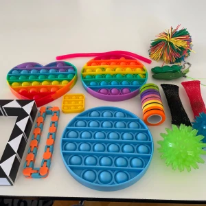 Fidget toys - Bilden visar en samling färgglada fidget-leksaker, inklusive pop-its, stressbollar och snurrande ringar. Perfekt för dig som gillar att hålla händerna sysselsatta, minska stress eller bara ha kul! Passar både ungdomar och unga vuxna som vill ha något roligt och avslappnande. Säljer för 80kr