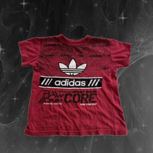 Röd Adidas baby t-shirt med tryck - Snygg röd t-shirt från Adidas med stort logotryck och grafiska detaljer på framsidan. T-shirten har rund hals, korta ärmar och är gjord i mjuk bomull. Perfekt för dig som gillar sportig streetstyle och vill sticka ut med en cool look. Barnstorlek men passar xs! 