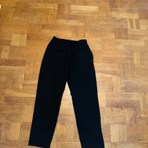 Zara Kostymbyxor (mjuka material)  - Svarta mjukisbyxor med elastisk midja och snörning framtill. Byxorna har raka ben och en enkel, clean look som passar perfekt för chill dagar. Materialet känns mjukt och bekvämt, och det finns fickor både fram och bak.