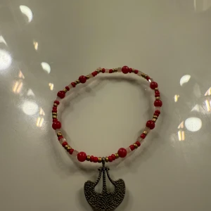 Rött pärlarmband med metallberlock - Snyggt armband med röda, vita och guldfärgade pärlor i olika storlekar. Armbandet har en unik metallberlock i form av en halvmåne med textur. Perfekt för dig som gillar färg och detaljer på handleden.