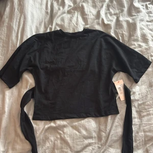 Svart T-shirt från nelly  - Svart T-shirt från nelly med knytning bak i ryggen. Helt ny med prislappen kvar och den är aldrig använd. Nypris 249kr