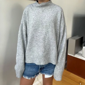 Grå stickad tröja - Mysig grå stickad polotröja med loose fit och ribbade muddar. Enkel och stilren design som funkar till jeans eller shorts.