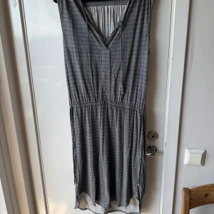 Svartvit mönstrad klänning S - Svartvit kortklänning med små geometriska mönster, v-ringad framtill och resår i midjan för en skön passform. Klänningen är ärmlös och tillverkad i mjuk viskos som känns lätt mot huden. Perfekt för dig som gillar stilrena detaljer och bekväma plagg.