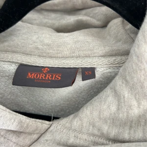 Beige hoodie från Morris  - Snygg beige hoodie från Morris med broderad logga på bröstet. Tröjan har ribbade muddar, mjukt material och klassisk passform. Perfekt för chill dagar och enkel att matcha med jeans eller joggers. Stl xs😁 använd max 10 ggr, passar dig som är runt 1,65