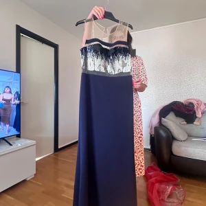 Marinblå långklänning med paljetter - Säljer en elegant marinblå långklänning med glittriga silverpaljetter upptill och transparent mesh vid axlarna. Klänningen har en rak, svepande siluett och är axelbandslös, perfekt för bal eller fest. Paljetterna ger en lyxig känsla och klänningen är riktigt snygg på.