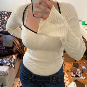 Ribbad vit långärmad tröja Gina Tricot - Supersnygg ribbad långärmad tröja från Gina Tricot i vit färg med svart kant runt den djupa, fyrkantiga halsringningen. Tröjan är slim fit och har långa ärmar med lite utsvängda muddar. Tyvärr så är den inte riktig gjord för folk med större bröst lol. Men den är jättesnygg och jag tror verkligen någon annan här kommer passa den perfekt :)
