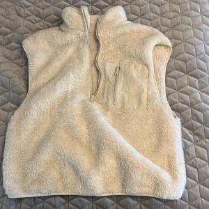 Vit fleeceväst med halv dragkedja - Mysig och fluffig vit fleeceväst med hög krage och halv dragkedja framtill. Västen har en praktisk bröstficka med dragkedja🤍