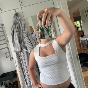 Vit ribbad ärmlös topp från Zara - Säljer en vit ribbad topp från Zara med fyrkantig urringning och bred halsringning som går runt nacken. Toppen är croppad och ärmlös, perfekt för en trendig och stilren look. Materialet är stretchigt och bekvämt.